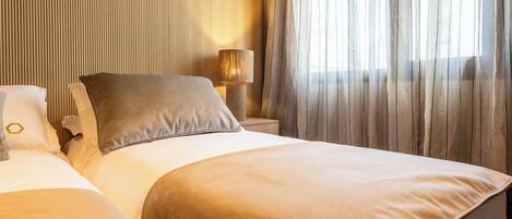 A hotel room with two beds, a nightstand, a lamp, and a large window with sheer curtains.