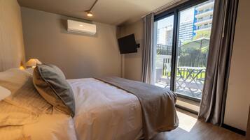A hotel room with a bed, a TV mounted on the wall, and a balcony with outdoor furniture.