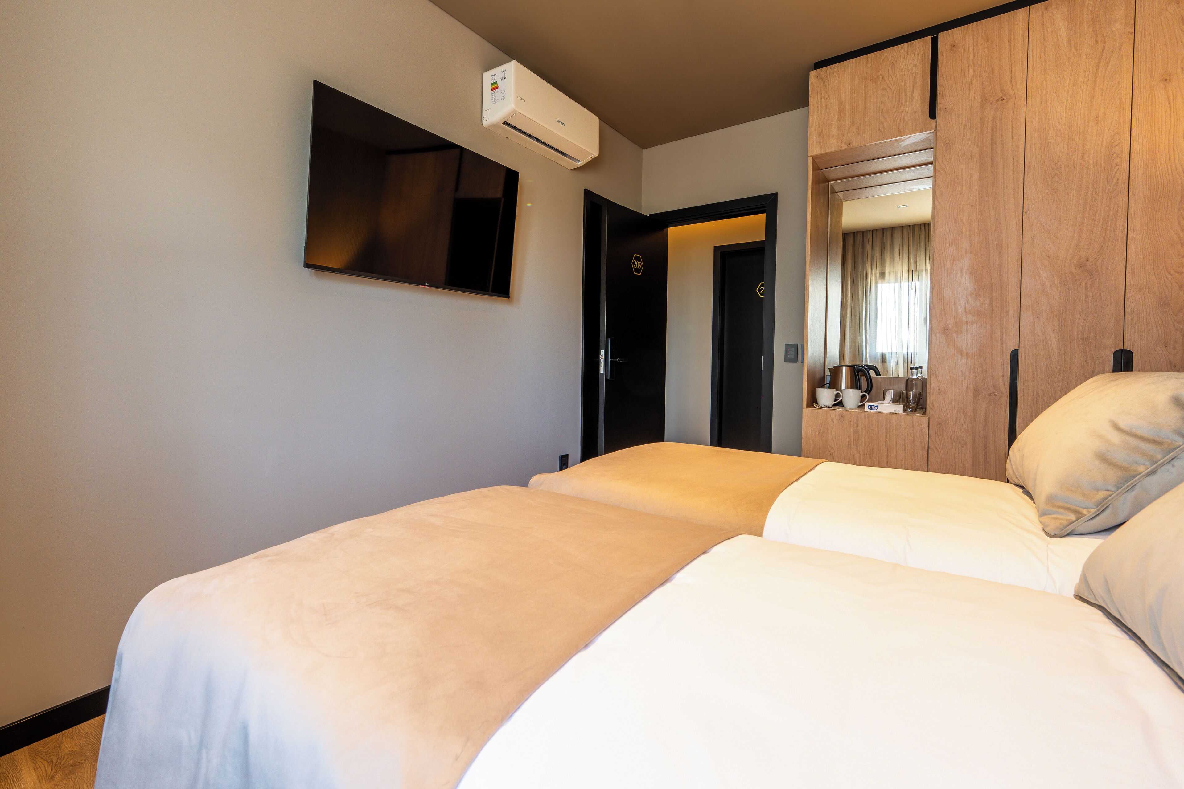 Habitación de hotel con dos camas, un televisor de pantalla plana montado en la pared y un armario con espejo.