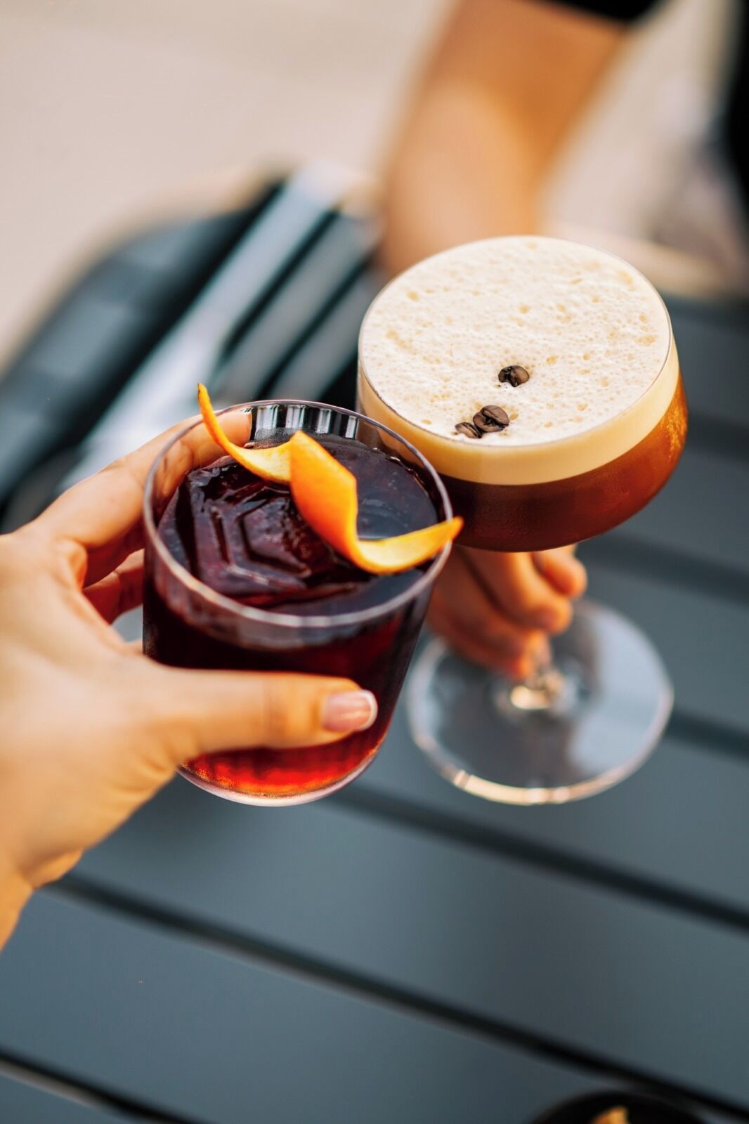 Two drinks in glasses, one dark and one light brown, with an orange garnish on the dark drink.