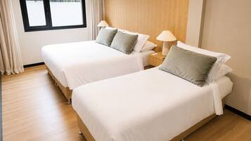 Habitación de hotel con dos camas individuales, cabecera de madera, ventana con cortinas y mesita de noche con lámpara.