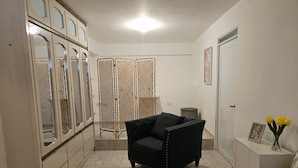 Une chambre à coucher avec un lit, un fauteuil noir, une armoire et une petite table sur laquelle est posé un vase de fleurs.