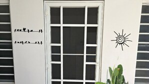 Une porte blanche ornée d’un motif quadrillé, un paillasson sur lequel est écrit « Bonjour, soleil », un cactus et un dessin de soleil sur le mur.