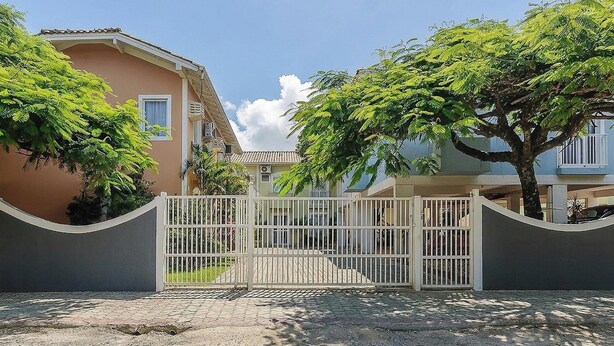 A residential building with a gated entrance, a paved driveway, and a clear sky. - CCM - Condominium 150m From Mariscal Beach (Bombinhas)