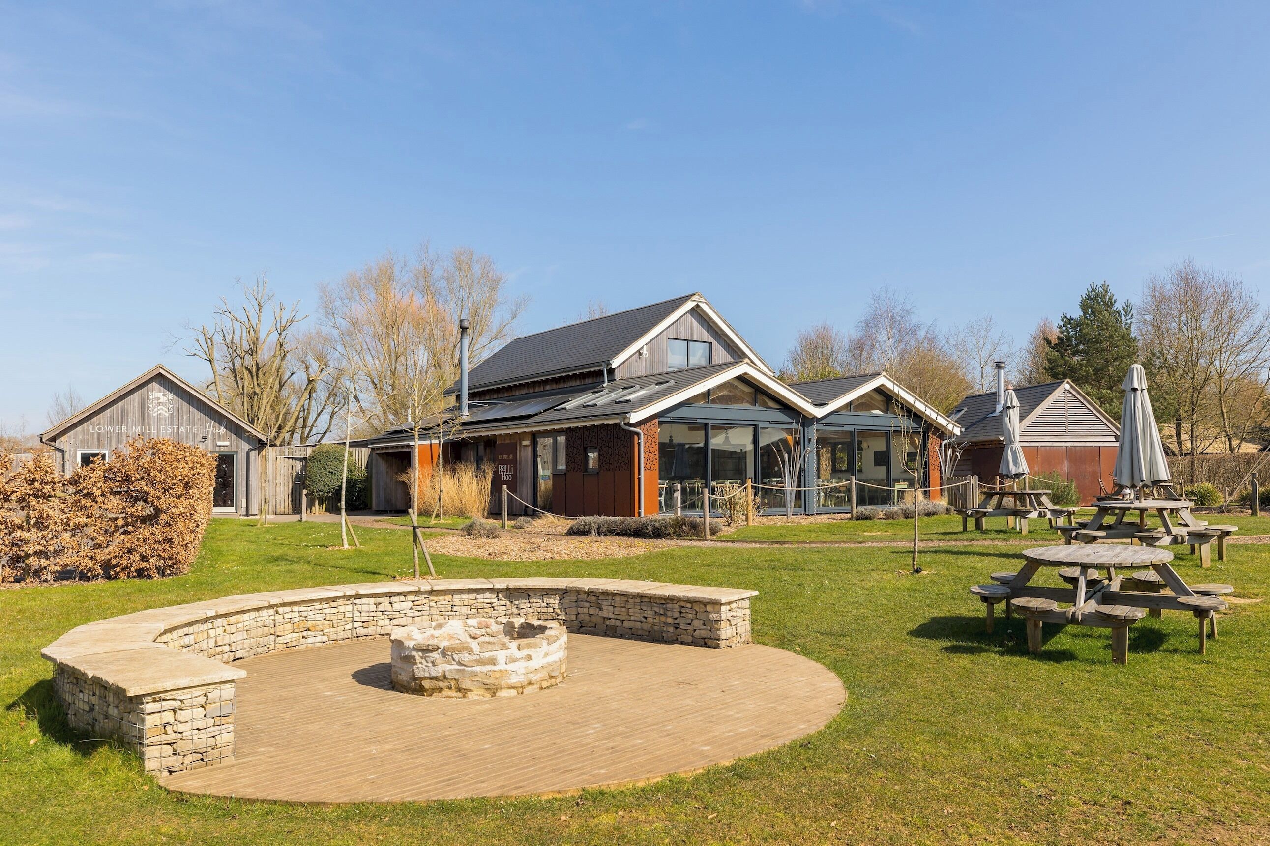 A residential property with a stone fire pit, picnic tables, and a well-maintained lawn.