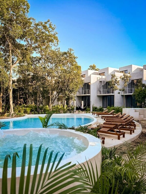 Ein Resort mit Poolbereich, Liegestühlen und einem modernen Gebäude mit Balkonen.