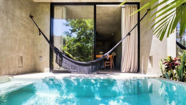 A swimming pool with a hammock and a sliding glass door leading to a dining area. - Seremonia Origen | Tú estudio con piscina privada (Tulum)