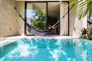 Una piscina con una hamaca y un ventanal corredera que da a un comedor.