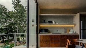 A modern kitchen with a built-in microwave, wooden cabinets, and a glass door leading to a balcony with a view of trees. - Seremonia Selva • Penthouse in the Jungle (Tulum)