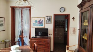 Un comedor con una mesa y sillas de madera, un televisor sobre un mueble de madera, una araña y una puerta que da a otra habitación.