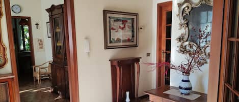 Un pasillo con suelo de madera, un banco de madera, un jarrón con flores rojas y un cuadro en la pared.