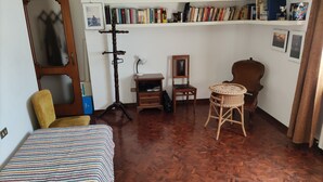 Una habitación con una cama, una silla, una mesita, una estantería y un espejo.