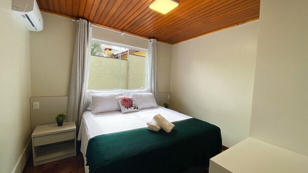 A neatly arranged bedroom with a bed, a bedside table, a small plant, and a window with curtains.