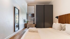 A modern bedroom with a large bed, a bedside table, a mirror, and a wardrobe.