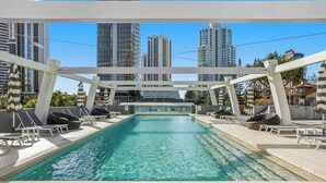 Una piscina en la azotea con sillones de descanso y sombrillas, rodeada de edificios modernos.