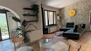 Un salon moderne avec une table à manger en verre entourée de chaises en bois, un mur d’accent en pierre et un canapé vert.