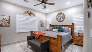 A bedroom with a wooden bed, a ceiling fan, and a large window with blinds.
