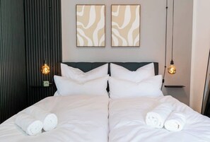A double bed with white linens, two wall-mounted light fixtures, and two abstract wall art pieces.