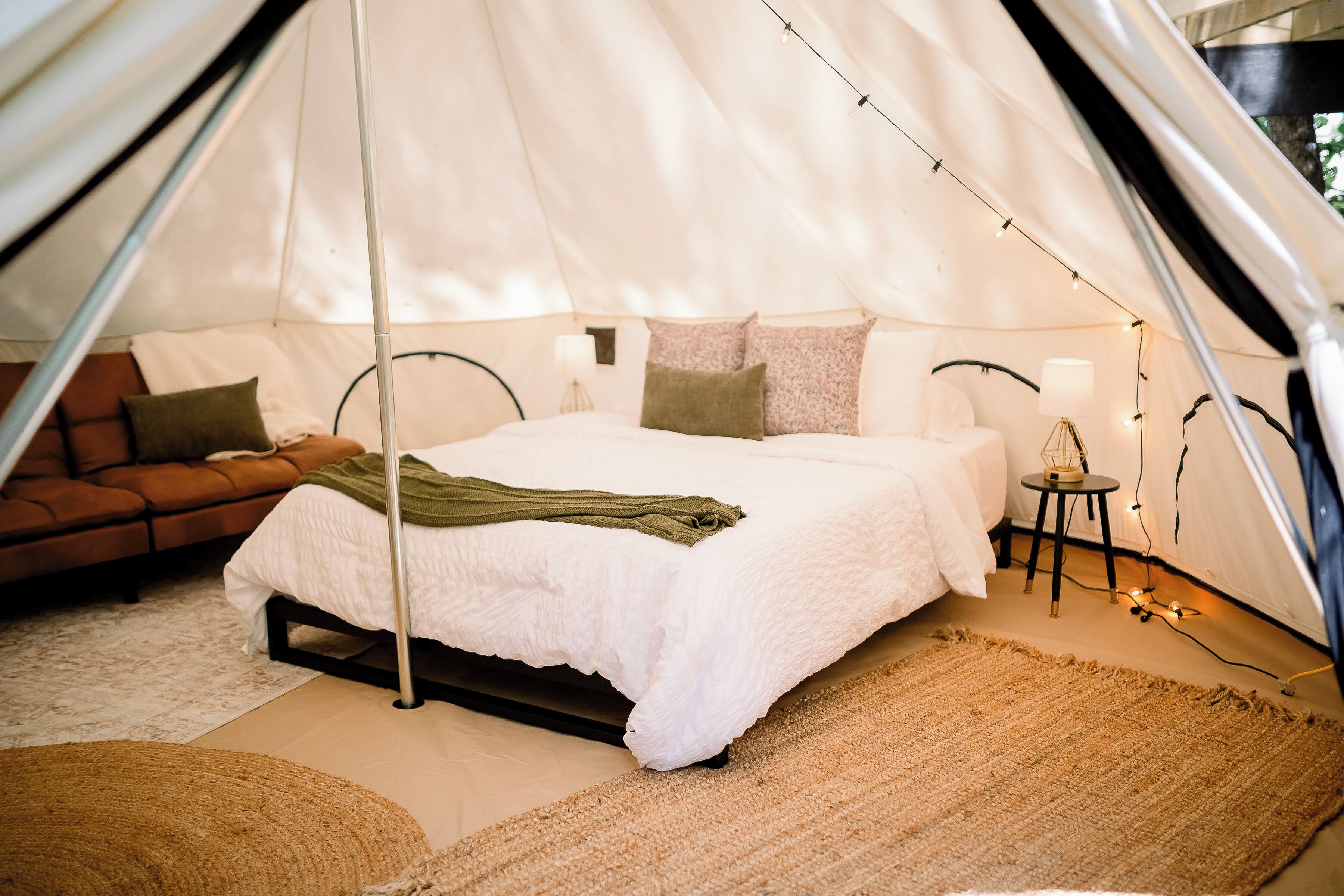 A tent with a bed, pillows, a small table with a lamp, and a sofa.
