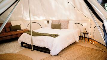 A tent with a bed, pillows, a small table with a lamp, and a sofa.