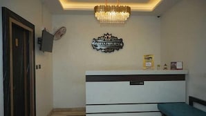Een receptiehal met een kroonluchter, een bord met de tekst 'Indian Imperial Hotel', een receptiebalie en een bank.