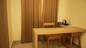 Een kleine kamer met een houten tafel en stoelen, een kastje en een gordijn.