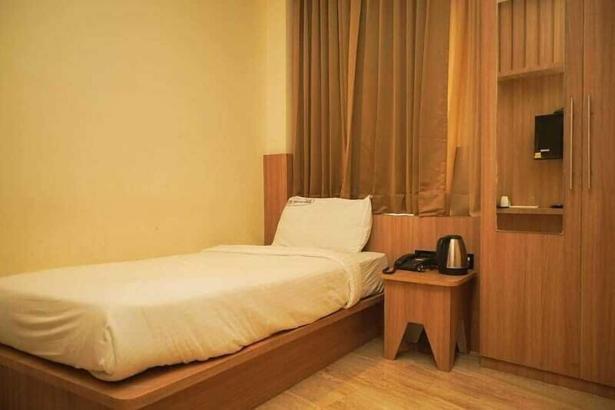 A single bed with a wooden frame, a bedside table with a kettle, and a small shelf with a mirror.