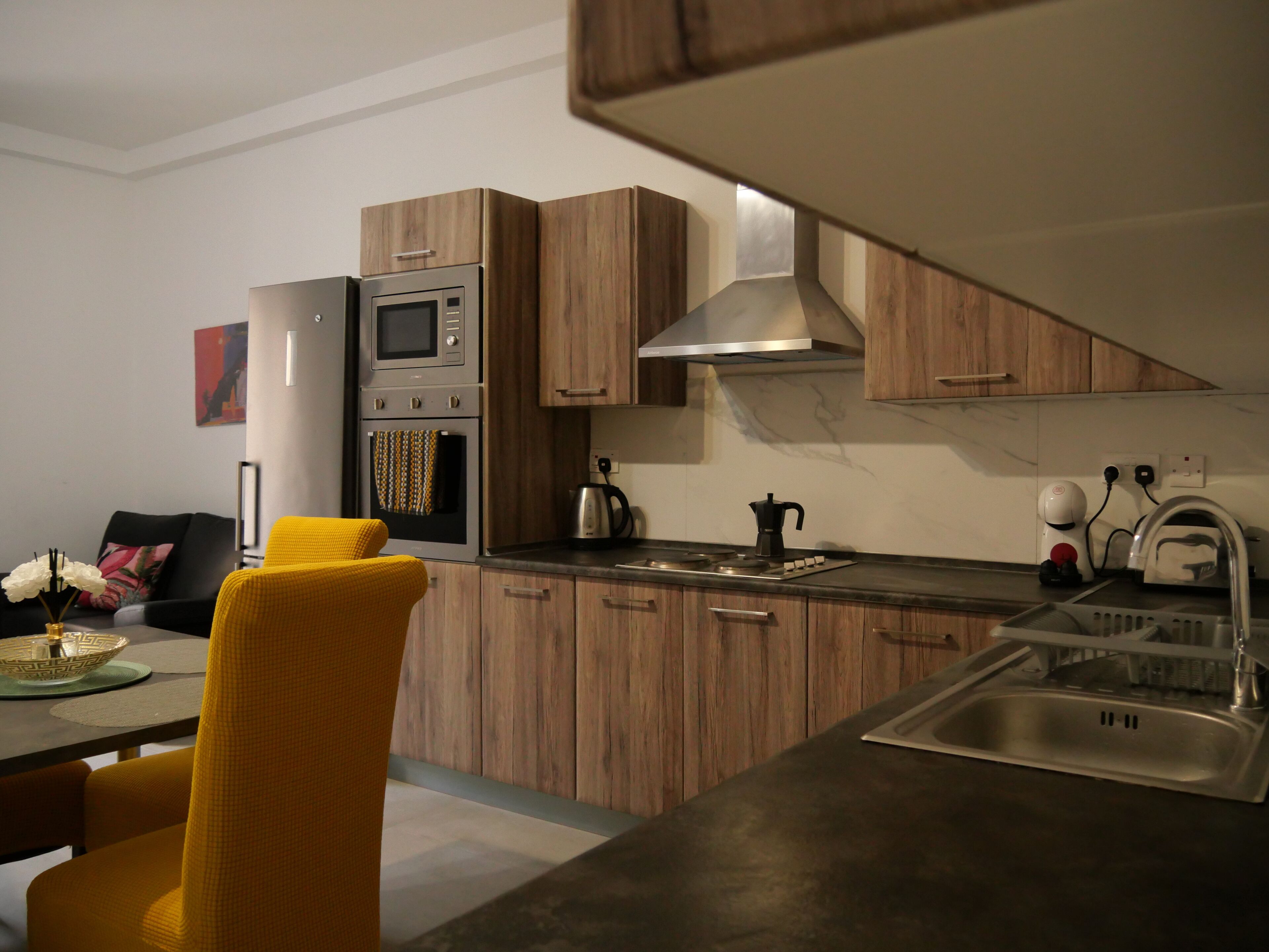 Una cocina moderna con armarios de madera, horno empotrado, microondas y pileta de acero inoxidable.