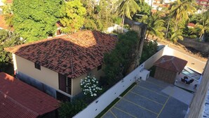 Un edificio con techo de tejas rojas, una zona de estacionamiento con líneas amarillas y vegetación circundante.