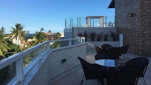 Una terrazza sul tetto con ringhiera in vetro, arredi da esterno e vista su palme e edifici.