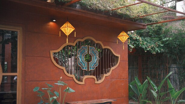 A rustic building with a large wooden bench, a decorative wall with a geometric pattern, and hanging lanterns. - DAINOI Hue Homestay (Hue)