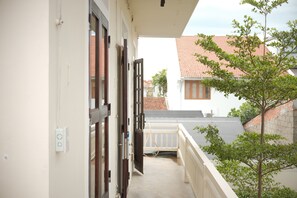 A balcony with a view of a red-tiled roof building, a tree, and a white railing.