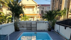 Ein rechteckiger Pool mit Fliesenrand, umgeben von einer niedrigen Mauer und einem Metallgitter.