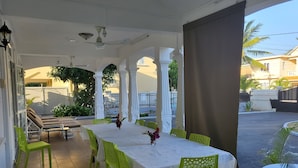 Ein überdachter Essbereich im Freien mit Tisch und Stühlen, einem Deckenventilator und Blick auf die umliegende Nachbarschaft.