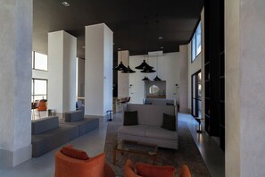 A spacious living area with a modern sofa, orange armchairs, and a coffee table. There are large windows providing natural light and a view of the outside. - Apto em Pinheiros c Piscina Academia e Smartlock (São Paulo)