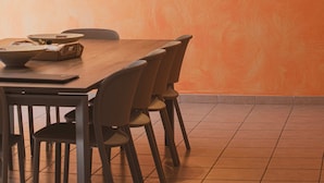 Een eethoek met een houten tafel en stoelen, een schilderij van een kustlandschap aan de muur, en een plafondlamp.