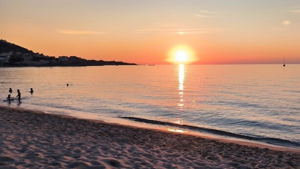 A beach at sunset with calm waters and a few people in the distance.