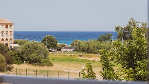 A balcony with a view of the sea, a building, and some greenery.