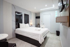 Una habitación de hotel moderna con una cama grande, una mesita de noche, un televisor montado en la pared y un pequeño escritorio con una silla.