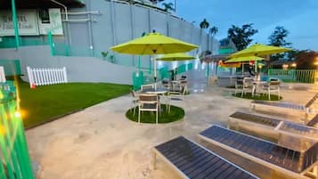 An outdoor patio area with tables and chairs, yellow umbrellas, and a poolside lounge area.