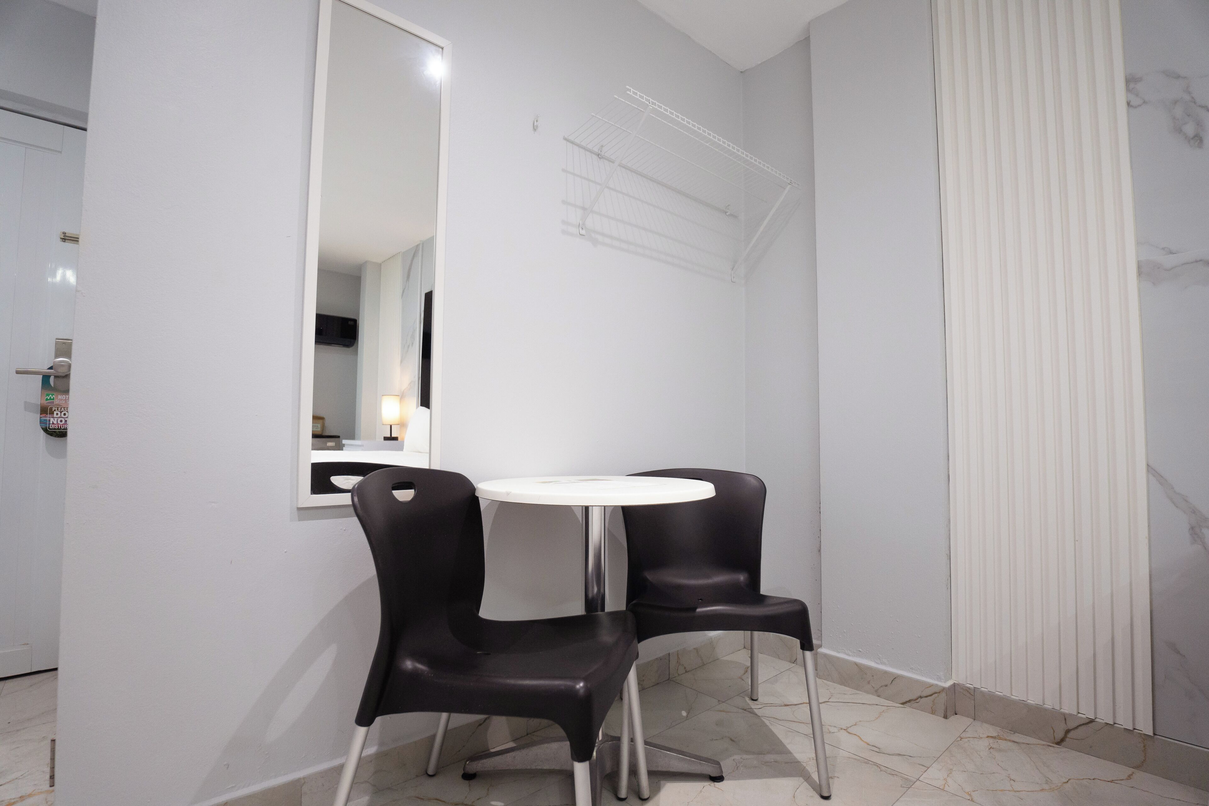 Une petite pièce moderne avec une table ronde blanche et deux chaises noires, un grand miroir et un radiateur blanc.