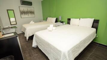 A hotel room with two beds, a desk, a trash bin, and a green accent wall.
