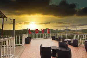 Una terraza con mobiliario de mimbre, barandal blanco y un letrero que dice 'LOVE'.