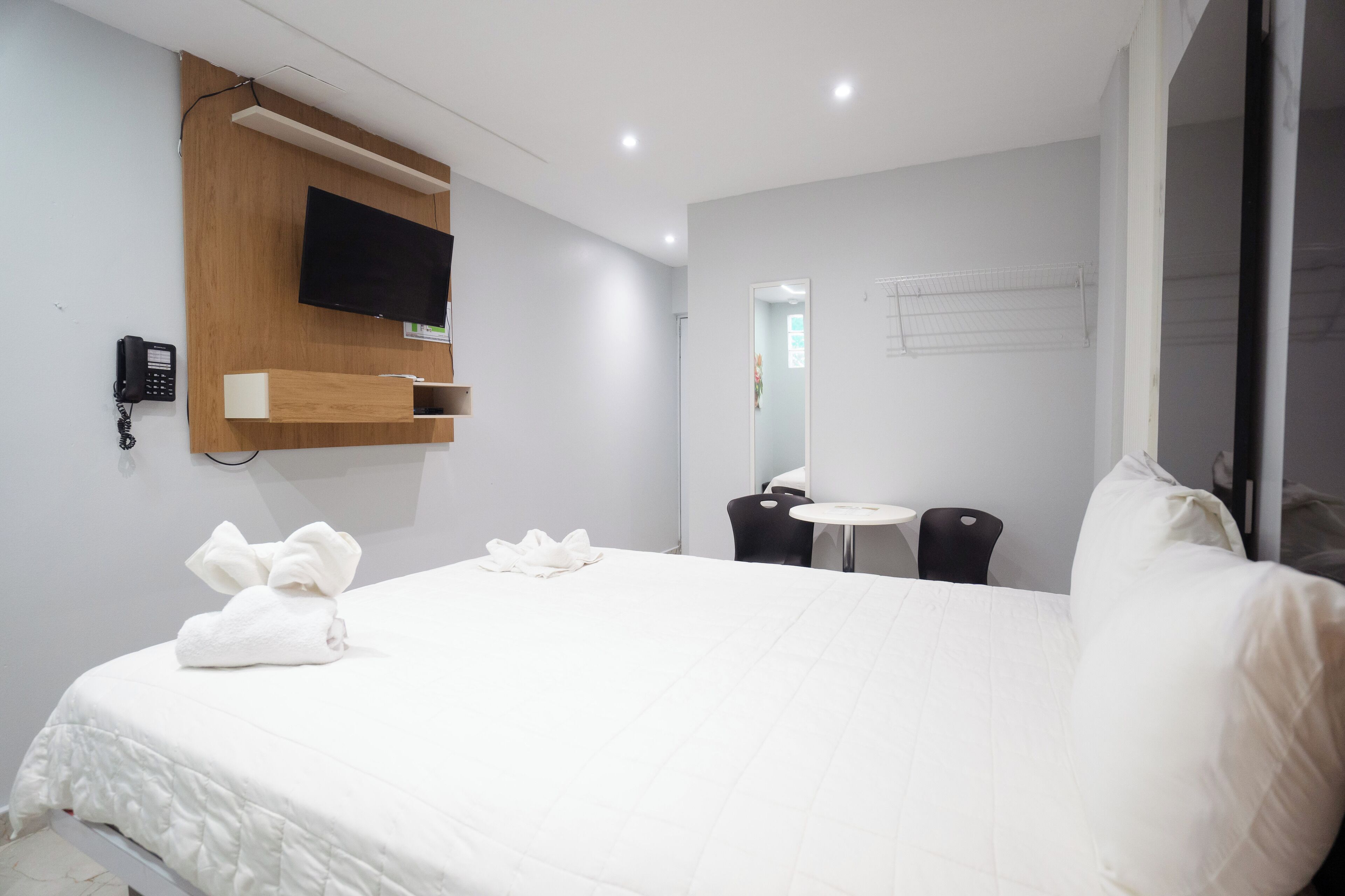 A hotel room with a large bed, a mounted TV, a desk with a chair, and a small table.
