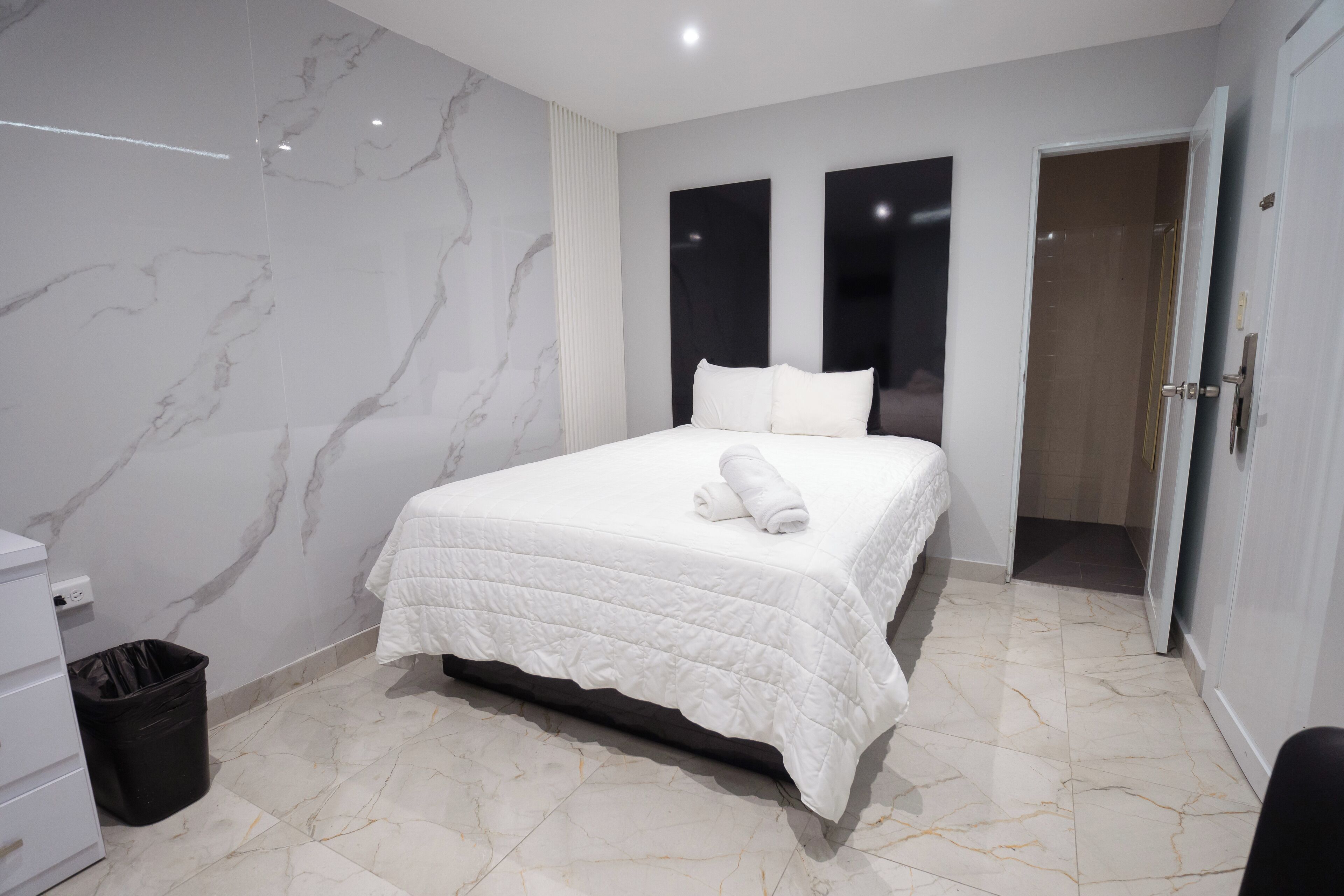 A modern hotel room with a marble floor, a neatly made bed with white bedding, and a black trash bin.