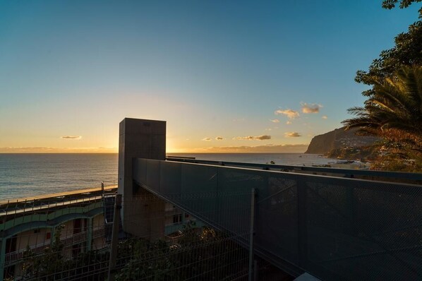 A coastal view with a building overlooking the sea, a clear sky, and a sunset.