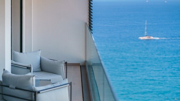 A balcony with a view of the sea, a chair, and a glass railing.