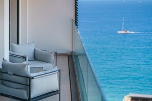 A balcony with a view of the sea, a chair, and a glass railing.