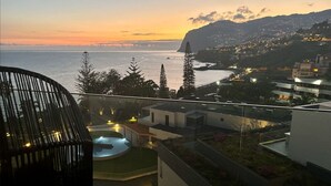 A balcony with a pool, overlooking a coastal cityscape at sunset.