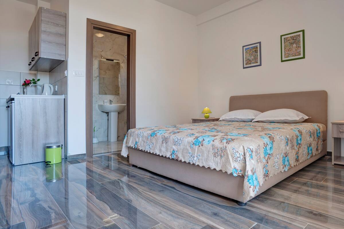 A bedroom with a bed, bedside tables, a nightstand, a sink, and a mirror.